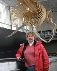 Susan Brown poses in a museum near a dinosaur skeleton.